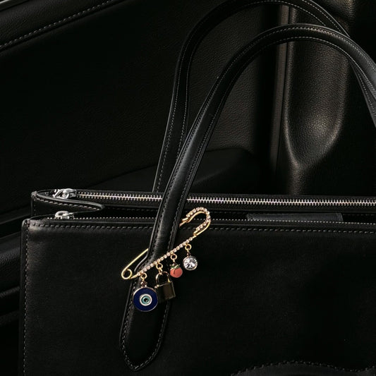 Gold purse charm with evil eye and heart charms clipped onto black leather handbag